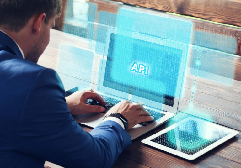 Mão de uma pessoa interagindo com uma superfície sensível ao toque, iluminada em tons de azul, sobre uma mesa escura. Ao redor da área de toque, aparecem várias interfaces digitais translúcidas flutuantes, conectadas por linhas, com gráficos e painéis de dados. Entre os elementos visíveis há gráficos de linha, barras e áreas, além de números e indicadores, como a sequência ‘1,524,894,783,825’. As cores variam entre azul, rosa, laranja e verde, destacando as diferentes visualizações. A iluminação cria contraste entre o brilho da interface e o ambiente escuro ao fundo, sugerindo análise de dados, visualização interativa e tecnologia avançada. (software)