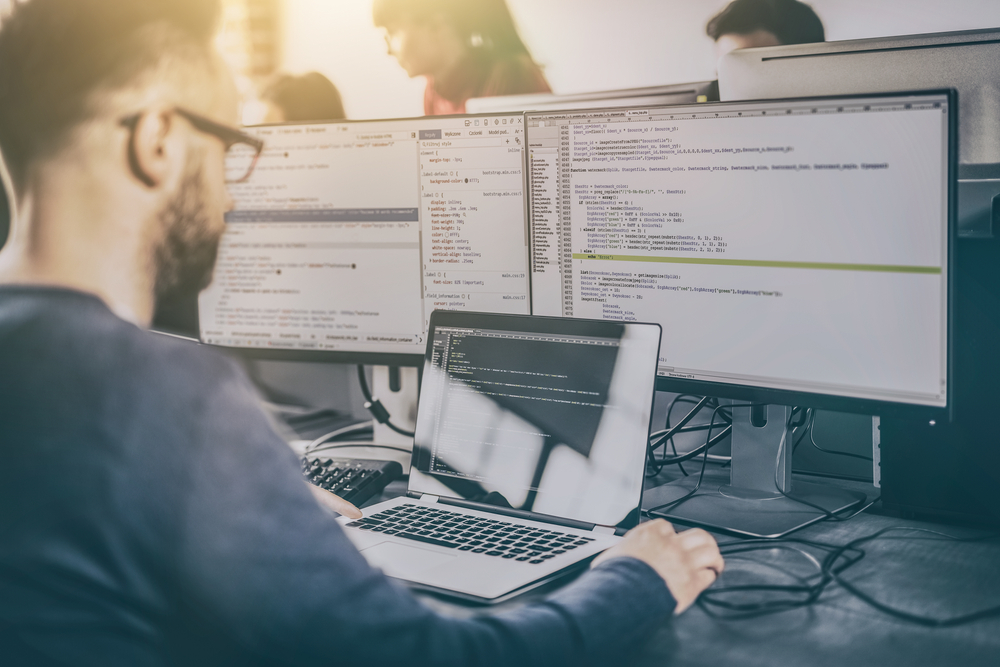 homem em frente a monitores trabalhando com códigos de programação