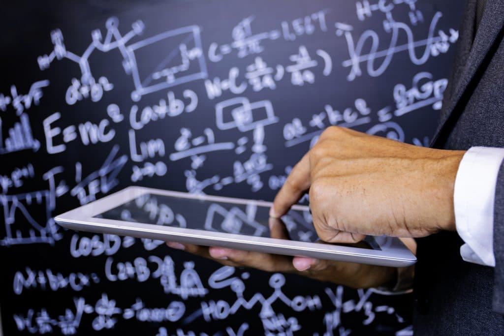 Close to the hand of the teacher using a tablet, Background is blackboard with a lot of mathematical formulas, The characters are glowing.