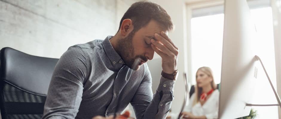 Young handsome frustrated and stressed businessman sitting at the office front a computer and holding head.