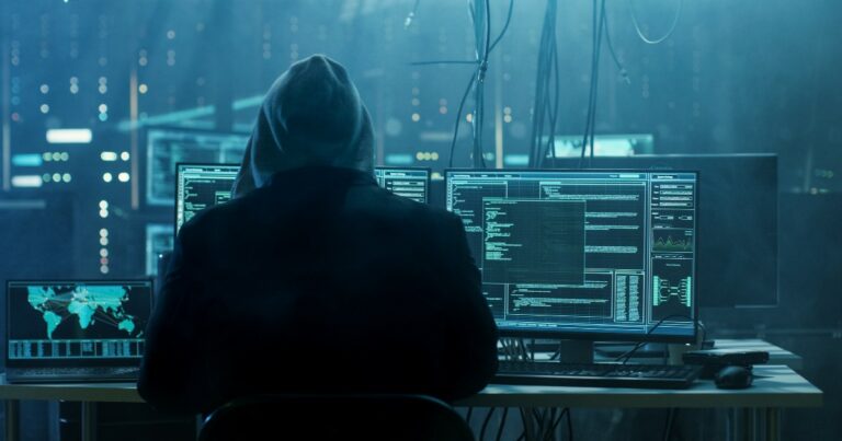Indivíduo sentado em frente a múltiplas telas de computador em um ambiente escuro, com códigos e mapas globais exibidos nas telas, representando atividades de hacking ou segurança cibernética (cibercriminosos, hacker, cibercrimes, hp crimes cibernéticos, setor financeiro, finanças, bancos, dados, man-in-the-middle, europol)