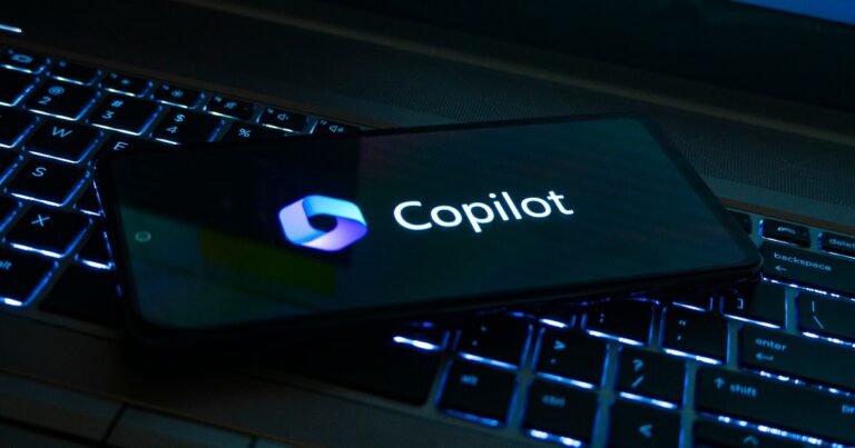 Imagem de um smartphone exibindo o logotipo e o nome 'Copilot', da Microsoft, posicionado sobre um teclado retroiluminado, representando inovação e integração tecnológica. (microsoft) (copilot)