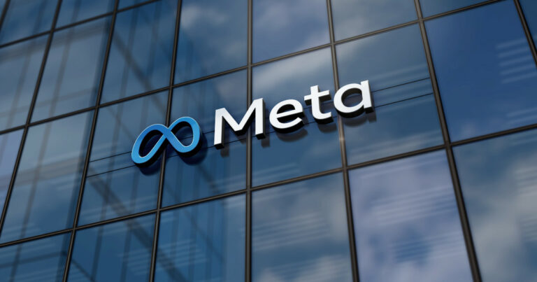A imagem mostra o logotipo da Meta, a empresa matriz do Facebook, exibido em uma fachada de vidro de um edifício moderno. O logotipo é composto por um símbolo em forma de infinito, em tons de azul, seguido pela palavra "Meta" em letras brancas e simples. O reflexo do céu e nuvens nas janelas do edifício cria um efeito visual interessante, destacando o logo de forma clara e moderna (Meta AI, Facebook, UE, Instagram, WhatsApp)