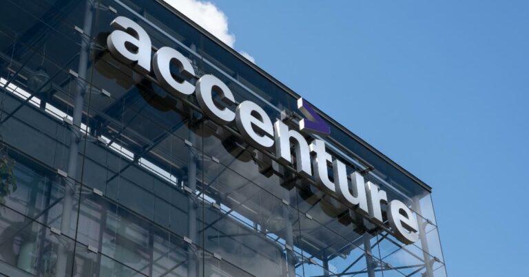 A imagem mostra a fachada de um edifício moderno com a logo da Accenture em destaque. O nome da empresa está escrito em letras brancas, com um acento circunflexo roxo acima da letra "t". A estrutura do prédio é de vidro e metal, refletindo o céu azul com algumas nuvens ao fundo (Accenture, inteligência artificial, aaru, europa, agêntica)