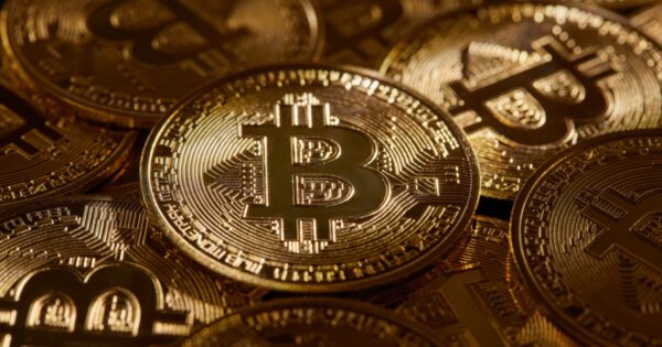 Imagem de moedas físicas de Bitcoin com design dourado, dispostas umas sobre as outras, refletindo a luz em seus detalhes e símbolos criptográficos (criptomoedas, Silvergate Bank, bitcoin)