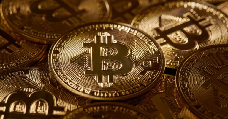 Imagem de moedas físicas de Bitcoin com design dourado, dispostas umas sobre as outras, refletindo a luz em seus detalhes e símbolos criptográficos (criptomoedas, Silvergate Bank, bitcoin)