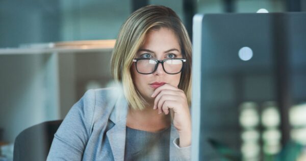 Mulher executiva de óculos, com expressão concentrada, analisando informações em uma tela de computador. Ela está em um ambiente de escritório moderno, vestindo um blazer cinza, transmitindo foco e profissionalismo (pensamento computacional, profissionais de TI, executiva, trabalho, mulher, trabalhadora, trabalhadores, profissionais, cresce, ia generativa)