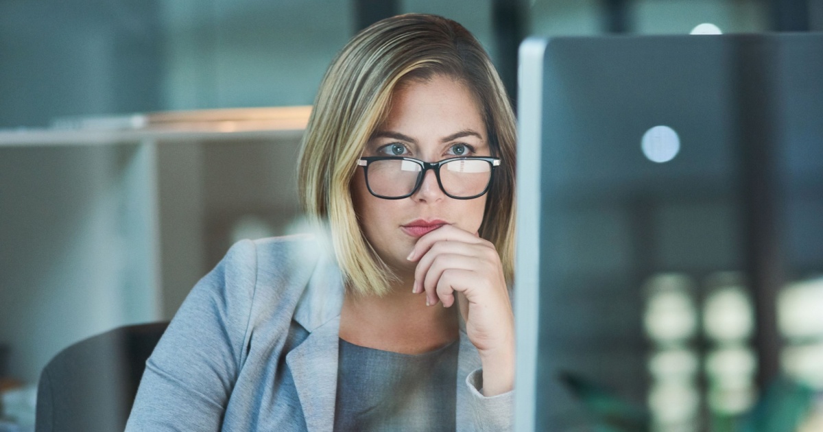 Mulher executiva de óculos, com expressão concentrada, analisando informações em uma tela de computador. Ela está em um ambiente de escritório moderno, vestindo um blazer cinza, transmitindo foco e profissionalismo (pensamento computacional, profissionais de TI, executiva, trabalho, mulher, trabalhadora, trabalhadores, profissionais, cresce, ia generativa)
