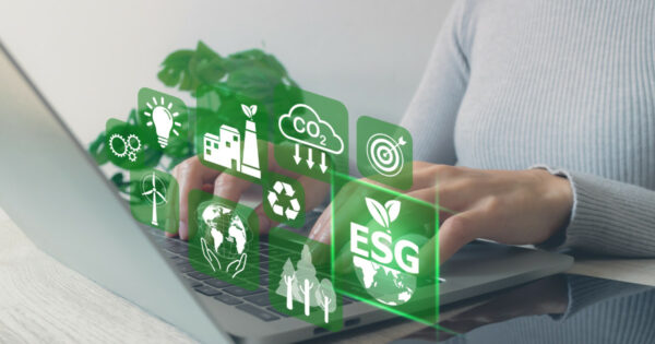 Pessoa usando um laptop com ícones digitais relacionados a ESG (Environmental, Social, and Governance) sobrepostos na imagem. Ícones incluem temas como energia renovável, emissão de CO₂, reciclagem, metas e sustentabilidade ambiental, empresa, stanford, biodiversidade