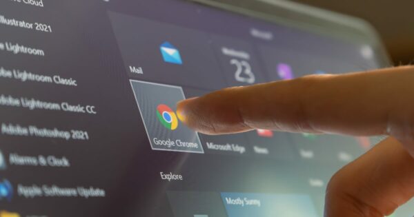 Dedo de uma pessoa tocando o ícone do navegador Google Chrome em uma tela de computador, que mostra vários ícones de aplicativos