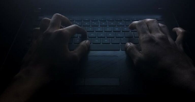 Mãos digitando em um teclado de laptop em um ambiente escuro, iluminadas por uma luz fraca que destaca o cenário misterioso e sombrio. A imagem evoca o conceito do lado obscuro da tecnologia, como cibercrimes ou atividades clandestinas, valor, tsmc