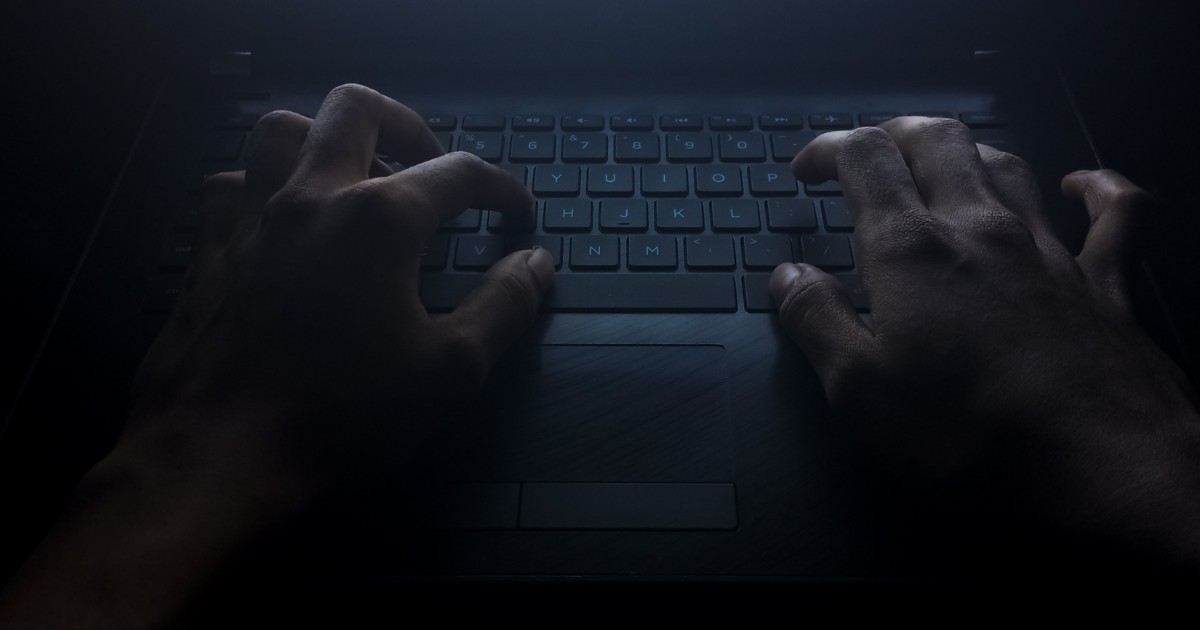 Mãos digitando em um teclado de laptop em um ambiente escuro, iluminadas por uma luz fraca que destaca o cenário misterioso e sombrio. A imagem evoca o conceito do lado obscuro da tecnologia, como cibercrimes ou atividades clandestinas, valor, tsmc
