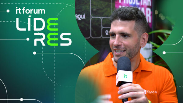 Imagem de Rodrigo Farah, head de marca de live commerce da Shopee, durante uma entrevista ao IT Forum Líderes. Ele veste uma camisa polo laranja com o logotipo da Shopee, segurando um microfone com o logo do IT Forum. O fundo destaca a identidade visual do evento, com detalhes modernos e vegetação