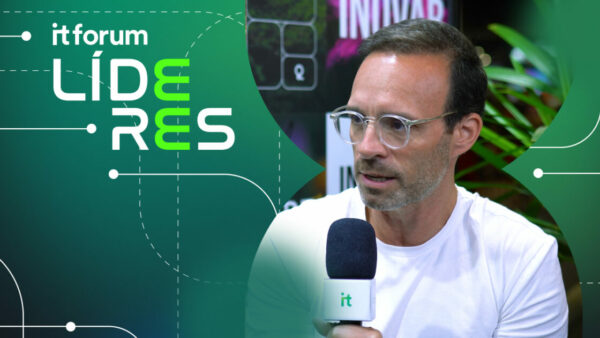 Imagem de Cristiano Nobrega, CDO da Totvs, sendo entrevistado no evento IT Forum Líderes. Ele veste uma camiseta branca e óculos de armação transparente, segurando um microfone com o logo do IT Forum. O fundo apresenta elementos visuais com a identidade do evento e vegetação ao redor