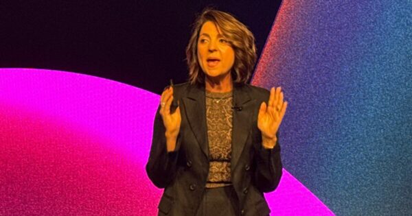 Paula Bellizia, VP Latam da AWS no reinvent 2024. Paula veste preto em um fundo roxo e rosa.