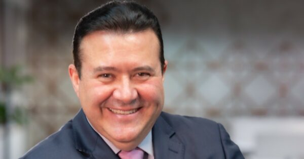 Imagem de Carlos Mauricio Ferreira, CEO da Positivo S+, sorrindo, usando terno e gravata, em um ambiente corporativo