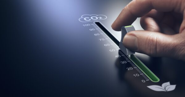 Uma mão ajustando um controle deslizante em uma interface digital, simbolizando a redução de emissões de CO2. O marcador está posicionado em torno de 40 em uma escala que vai de 0 a 100, com um indicador verde representando sustentabilidade. No canto inferior direito, há um ícone de folha, reforçando o tema de preservação ambiental e ESG. O fundo é escuro, destacando o controle iluminado. (co2, emissoes, gases, efeito estufa, ESG, sustentabilidade, IA generativa, genai, investimentos)