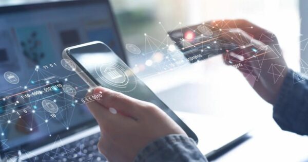 Pessoa segurando um smartphone e um cartão de crédito, com elementos gráficos digitais representando transações financeiras, tecnologia bancária e conexões de dados. Ao fundo, um notebook desfocado. A imagem simboliza fintechs, digitalização de serviços financeiros e pagamentos online (fintech, finanças, bancarização, cartão, serviços financeiros, setor financeiro, cartões, pagamentos, giro)