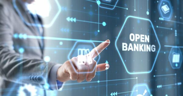 Imagem conceitual sobre Open Banking. Uma mão apontando para um painel digital com o texto 'OPEN BANKING' destacado em um hexágono luminoso. O fundo apresenta ícones tecnológicos e conexões digitais em tons de azul, representando a integração e o compartilhamento de dados financeiros de forma segura e transparente, consentimentos (fintech, open finance)