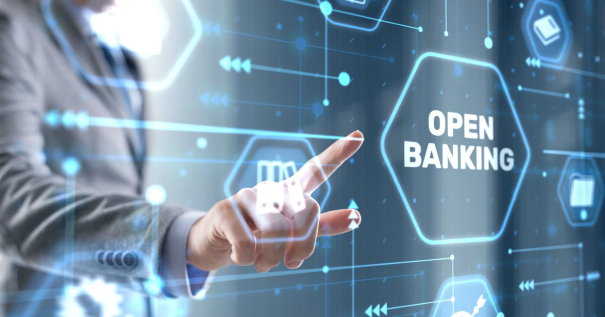 Imagem conceitual sobre Open Banking. Uma mão apontando para um painel digital com o texto 'OPEN BANKING' destacado em um hexágono luminoso. O fundo apresenta ícones tecnológicos e conexões digitais em tons de azul, representando a integração e o compartilhamento de dados financeiros de forma segura e transparente, consentimentos (fintech, open finance)