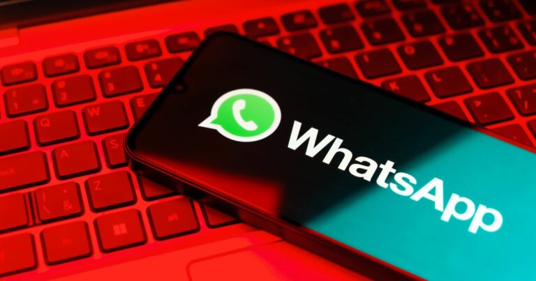 Imagem de um smartphone com o logótipo do WhatsApp no ecrã, apoiado sobre o teclado de um portátil iluminado por luz vermelha intensa. O contraste entre a iluminação vermelha e o fundo verde da aplicação destaca o ícone da mensagem dentro de um balão de fala, símbolo reconhecível da plataforma. banco, malware