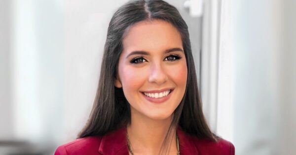 Renata Koch Alvarenga, fundadora da EmpoderaClima, aparece sorrindo em um retrato profissional. Ela está com os cabelos soltos e lisos, veste um blazer vermelho e está diante de um fundo neutro e claro, que destaca seu rosto (líder)