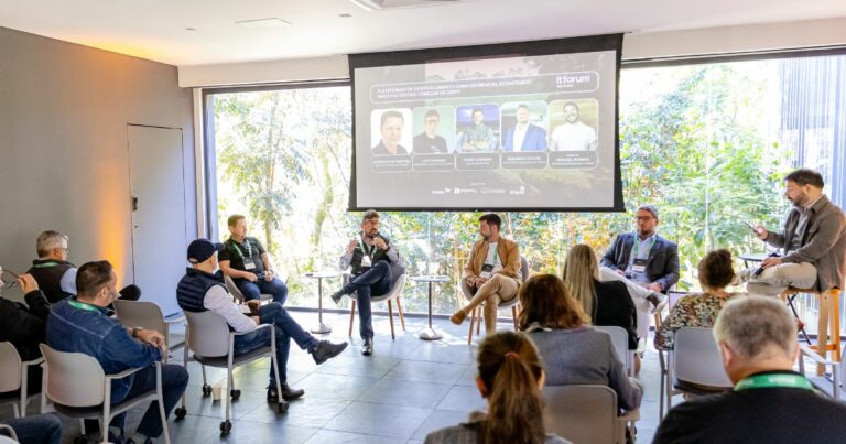 Painel de discussão com vários oradores sentados em cadeiras diante de um ecrã com informações sobre o tema do evento do itforum, enquanto a audiência assiste atentamente numa sala iluminada por luz natural (executivos, Na Mata, IT Forum)
