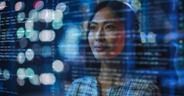 Imagem de uma mulher olhando pensativamente através de uma tela de vidro com códigos de programação projetados sobre ela, simbolizando o uso de inteligência artificial e tecnologia. O fundo apresenta luzes desfocadas, reforçando o ambiente tecnológico e moderno. A expressão da mulher transmite foco e reflexão (pensamento, meta, ia)