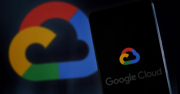 Imagem de um smartphone com a tela exibindo o logotipo do Google Cloud, composto por uma nuvem estilizada com as cores azul, vermelho, amarelo e verde características do Google. Ao fundo, o mesmo logotipo aparece em tamanho ampliado e desfocado, compondo o fundo escuro da imagem. A palavra “Google Cloud” aparece parcialmente na parte inferior da tela do celular. A composição destaca o tema de serviços em nuvem e tecnologia (governança)