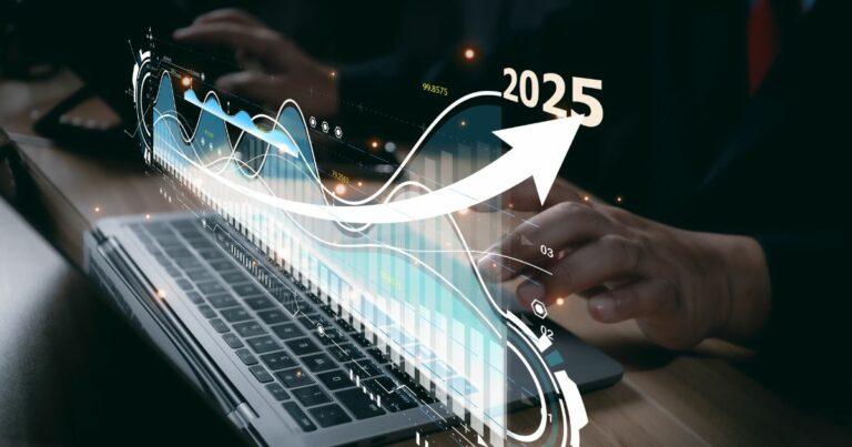 Uma pessoa está digitando em um teclado de laptop, enquanto uma sobreposição gráfica aparece na tela. Essa sobreposição exibe elementos visuais relacionados à análise de dados e projeções de crescimento financeiro, incluindo linhas, gráficos de barras e uma seta apontando para cima. No canto superior direito, destaca-se o ano "2025", e há também valores numéricos visíveis, como "99.8575", sugerindo métricas ou indicadores de desempenho.