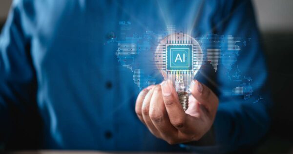 Pessoa vestindo camisa azul segura uma lâmpada acesa com o símbolo “AI” (inteligência artificial) no centro, estilizado como um chip de computador. Ao fundo, há uma representação digital do mapa-múndi com elementos gráficos que sugerem tecnologia e conectividade global, retorno, parceria (consciênte, startups, decisão, generativa, industria, processo, gratuitas, tendências, serviço)