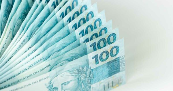 Notas de cem reais do Brasil dispostas em leque, com destaque para o número “100” e a figura do rosto da efígie da República nas cédulas, crédito
