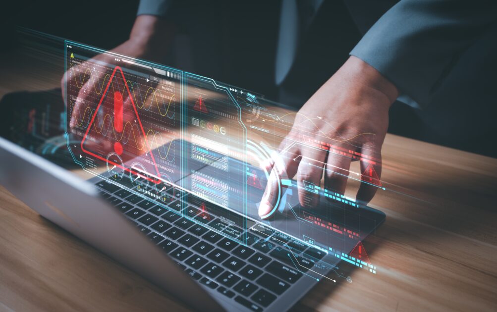 Imagem de um profissional de cibersegurança monitorando sistemas e monitorando alertas em uma tela holográfica, destacando a importância da proteção digital.