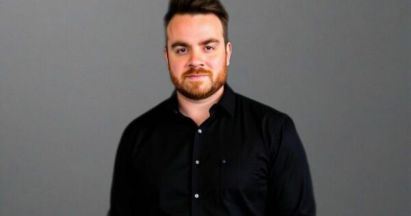 Pólen Kuhnen, country manager da CM Mobile, vestindo uma camisa preta de botões está posicionada diante de um fundo cinza liso. Não há outros elementos visuais ou texto na imagem.