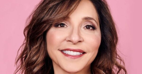 Uma pessoa com cabelo ondulado na altura dos ombros aparece em frente a um fundo rosa. (Linda, ex-CEO do X)