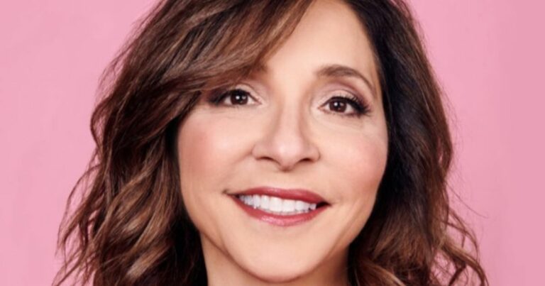 Uma pessoa com cabelo ondulado na altura dos ombros aparece em frente a um fundo rosa. (Linda, ex-CEO do X)