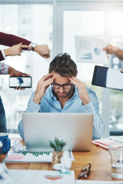 Pessoa estressada no escritório com várias mãos apontando para ela, simbolizando pressão no trabalho, frustração e ansiedade. (segurança)