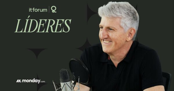 Homem de cabelos grisalhos e camiseta preta sorri enquanto participa de uma gravação com microfone e pop filter à frente. Ao fundo, sobre um fundo escuro, estão os textos "it forum", "LÍDERES" e o logotipo da empresa monday.com. A imagem está relacionada ao programa "IT Forum Líderes" e mostra Maurício Prado, que é o foco da entrevista ou participação.