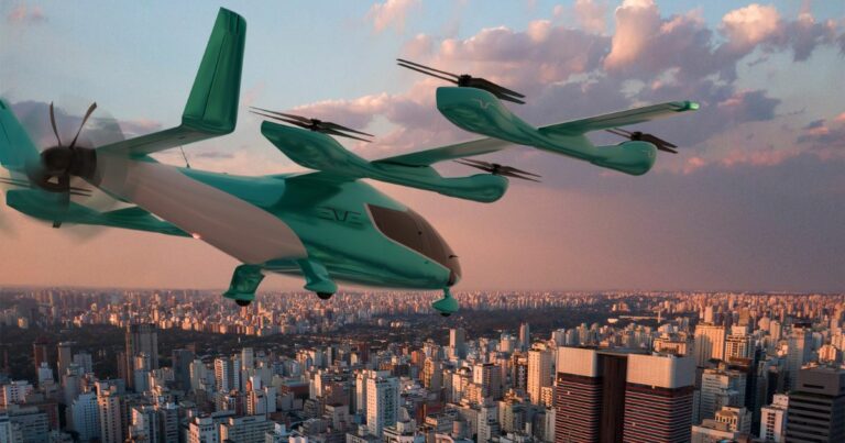 Uma aeronave elétrica de decolagem e pouso vertical (eVTOL), na cor verde-azulada, está voando sobre uma cidade densamente povoada, com muitos prédios altos. O céu está parcialmente nublado, com tons quentes de laranja e rosa, sugerindo o nascer ou o pôr do sol. (Eve)