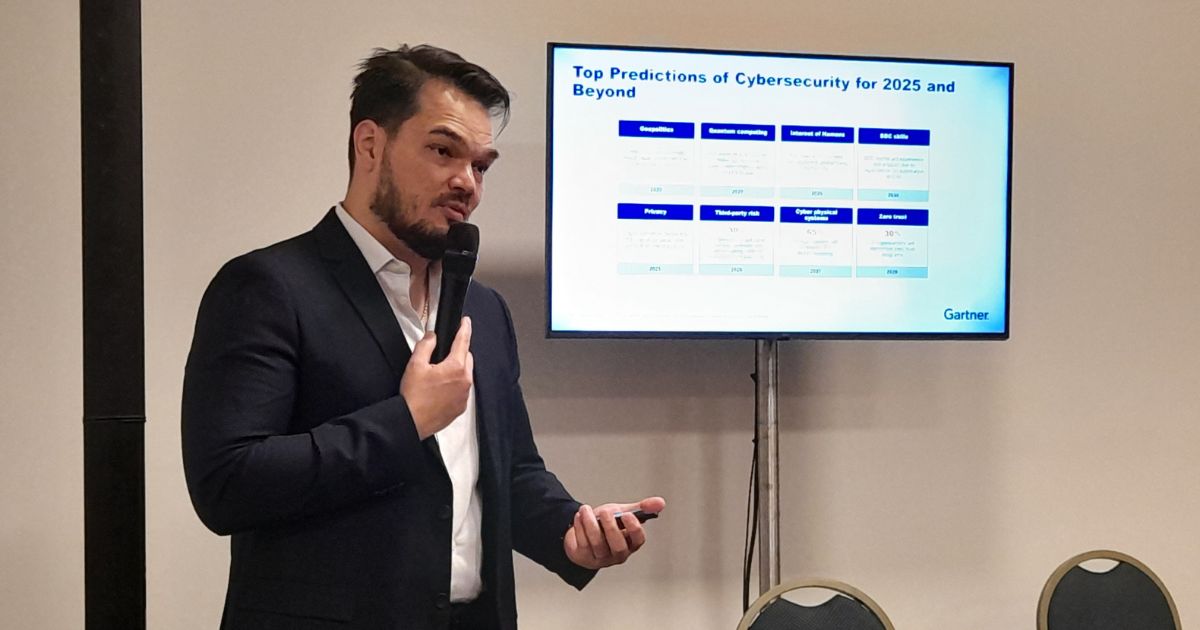 Uma pessoa vestida com terno segura um microfone enquanto apresenta diante de uma tela. A tela exibe o título “Top Predictions of Cybersecurity for 2025 and Beyond” com várias previsões listadas abaixo. Embora o texto completo não seja legível, é possível identificar colunas com os títulos “Prediction”, “Description” e outras relacionadas a previsões de cibersegurança. Há também uma tabela à direita com informações detalhadas. (gartner)
