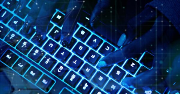 Simulação de cibercrime com imagem em close-up de mãos digitando em um teclado retroiluminado com luz azul. As teclas estão iluminadas e os dedos estão posicionados sobre diferentes teclas. (Anthropic, coding)