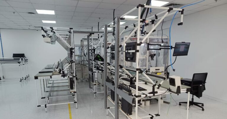 Linha de montagem automatizada em uma fábrica da Lenovo, com esteiras, monitores, estruturas metálicas e equipamentos de alta tecnologia organizados em ambiente limpo e iluminado.