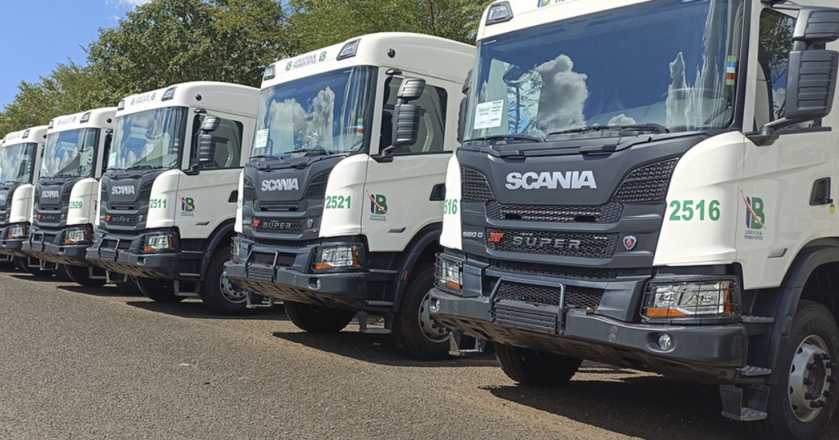 Fila de caminhões brancos da marca Scania, estacionados lado a lado, com a logo da empresa **I.B Logística e Transportes** estampada nas portas (reduz)