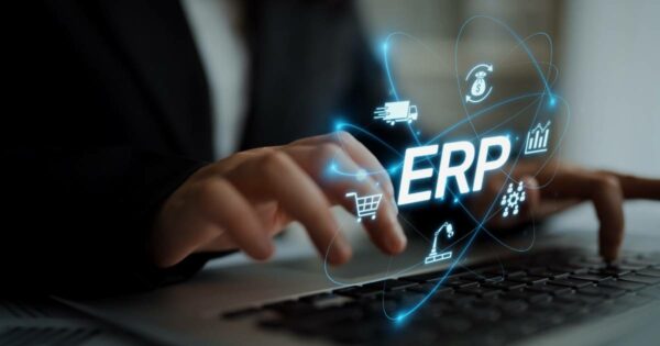 Pessoa digitando em um laptop, com a palavra “ERP” em destaque sobreposta à imagem, cercada por ícones digitais que representam logística, finanças, compras, produção e gestão de dados. Representação do uso de sistemas ERP na administração empresarial. (TK Elevator)