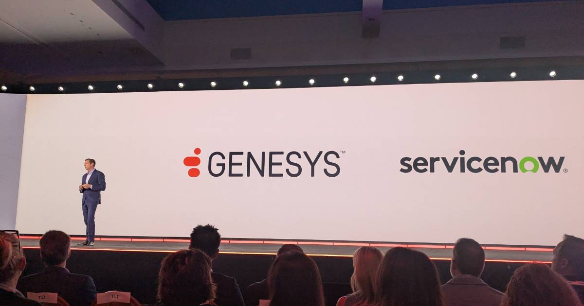 Homem de terno azul, identificado como Tony Bates, CEO da Genesys, está em um palco apresentando diante de um grande telão com os logotipos da Genesys e da ServiceNow. Na frente, várias pessoas assistem à apresentação.