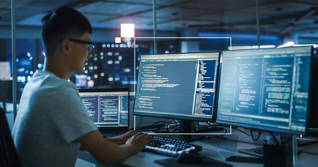 Pessoa desenvolvedora de software trabalhando com AI PCs com múltiplas telas de código em ambiente de escritório à noite. Brasil (IA)
