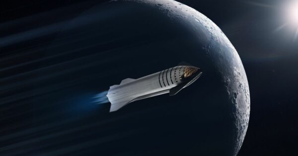 A imagem mostra uma espaçonave voando próxima à Lua, com seus motores emitindo um brilho azul. A Lua está parcialmente iluminada, e o Sol aparece ao fundo, projetando luz sobre a nave e a superfície lunar. A cena representa exploração espacial e tecnologia avançada. (SpaceX)