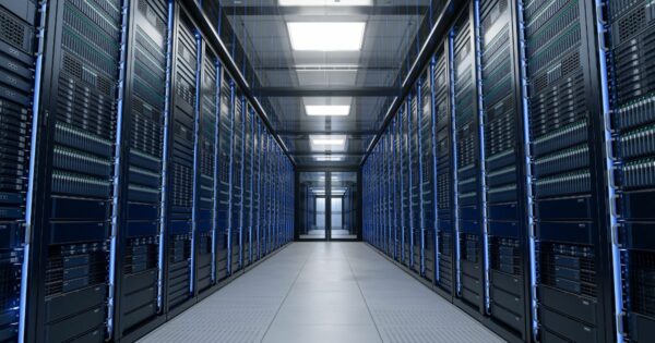 A foto mostra o interior de um corredor de data center, com fileiras de racks de servidores alinhadas dos dois lados. Cada rack contém múltiplos equipamentos eletrônicos organizados verticalmente, com luzes indicadoras verdes e azuis acesas. O ambiente é iluminado por painéis de luz no teto, refletindo no piso claro e criando uma aparência limpa e moderna. A perspectiva central dá profundidade à imagem, destacando a simetria e a infraestrutura tecnológica. (IEA), computação, legrand, para representar futuro data center da Huge Networks