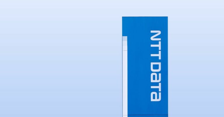 A imagem apresenta um painel vertical azul com o logotipo e o nome NTT DATA em letras brancas, dispostos na orientação vertical. O fundo é minimalista, com um tom uniforme de azul claro, criando um contraste limpo e moderno com o painel. Esse tipo de imagem transmite identidade corporativa forte, tecnologia e inovação, sendo ideal para materiais institucionais, apresentações ou posts relacionados à marca e seus serviços.