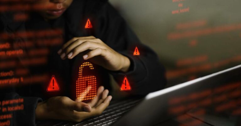 Pessoa parcialmente visível usando laptop no escuro, com as mãos em volta de um ícone digital de cadeado aberto iluminado em vermelho, cercado por símbolos de alerta, representando vazamento de dados ou falha de segurança (paralisa, dataprev)